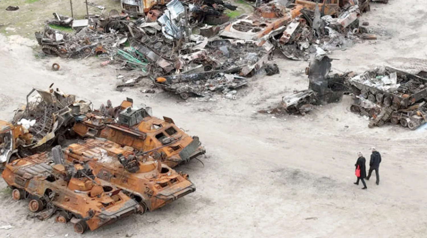 شخصان يمرّان قرب عربات عسكرية مدمرة في بوتشا بضواحي كييف أمس (أ.ب)