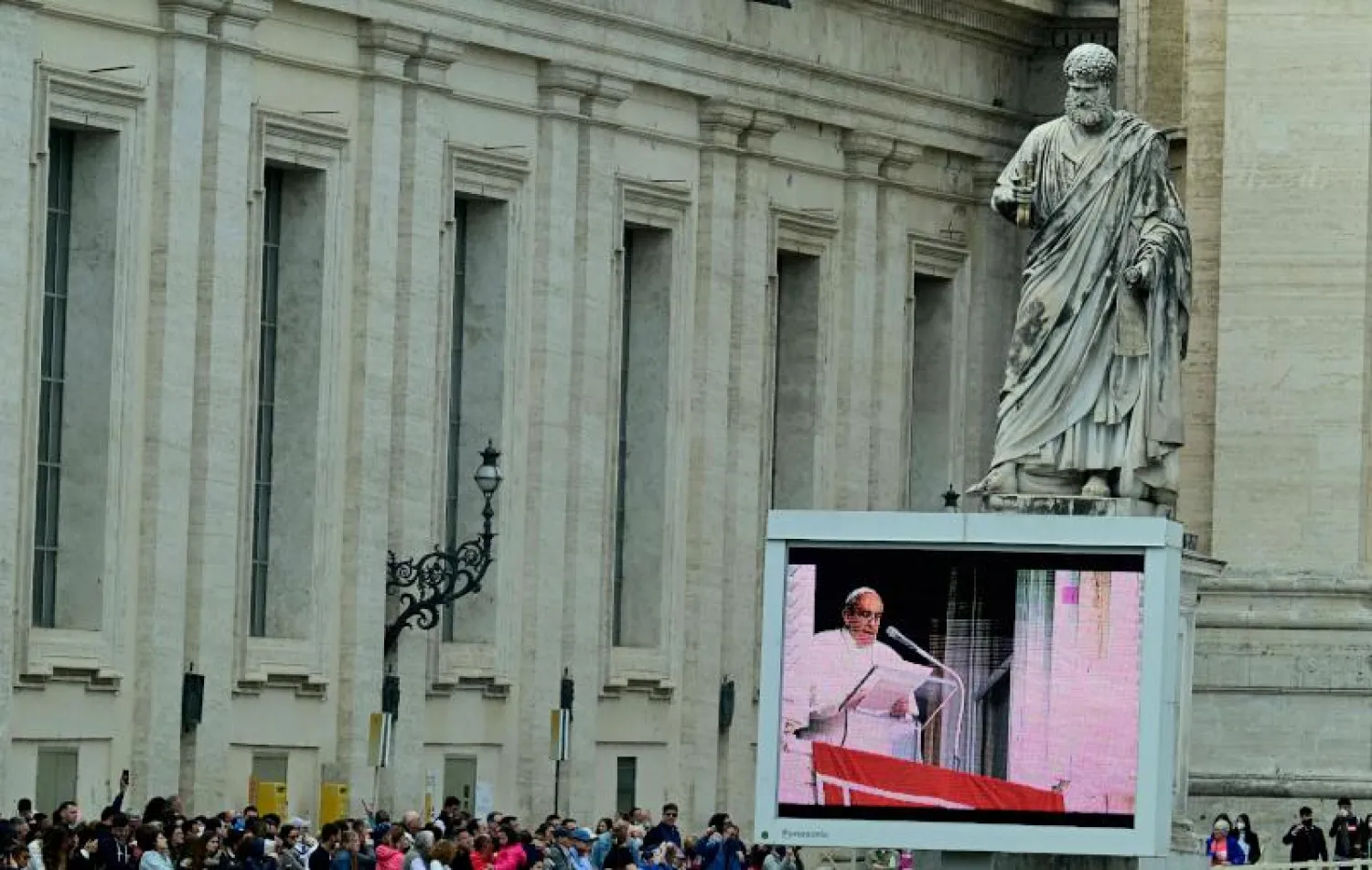 شاشة تعرض كلمة البابا فرنسيس أسفل تمثال القديس بطرس في ساحة الفاتيكان (أ.ف.ب)