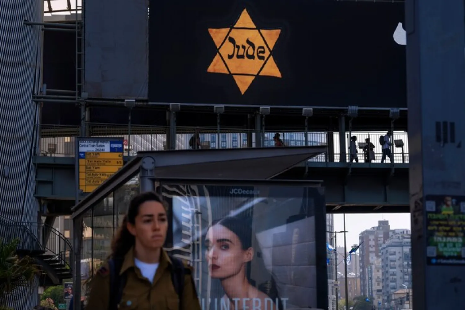 People walk along a bridge lit with a billboard showing a yellow Star of David that reads “Jude”, Jew in German, resembling the one Jews were forced to wear in Nazi Germany, during the annual Holocaust Remembrance Day in Ramat Gan, Israel, Thursday, April 28, 2022. (AP Photo/Oded Balilty)

