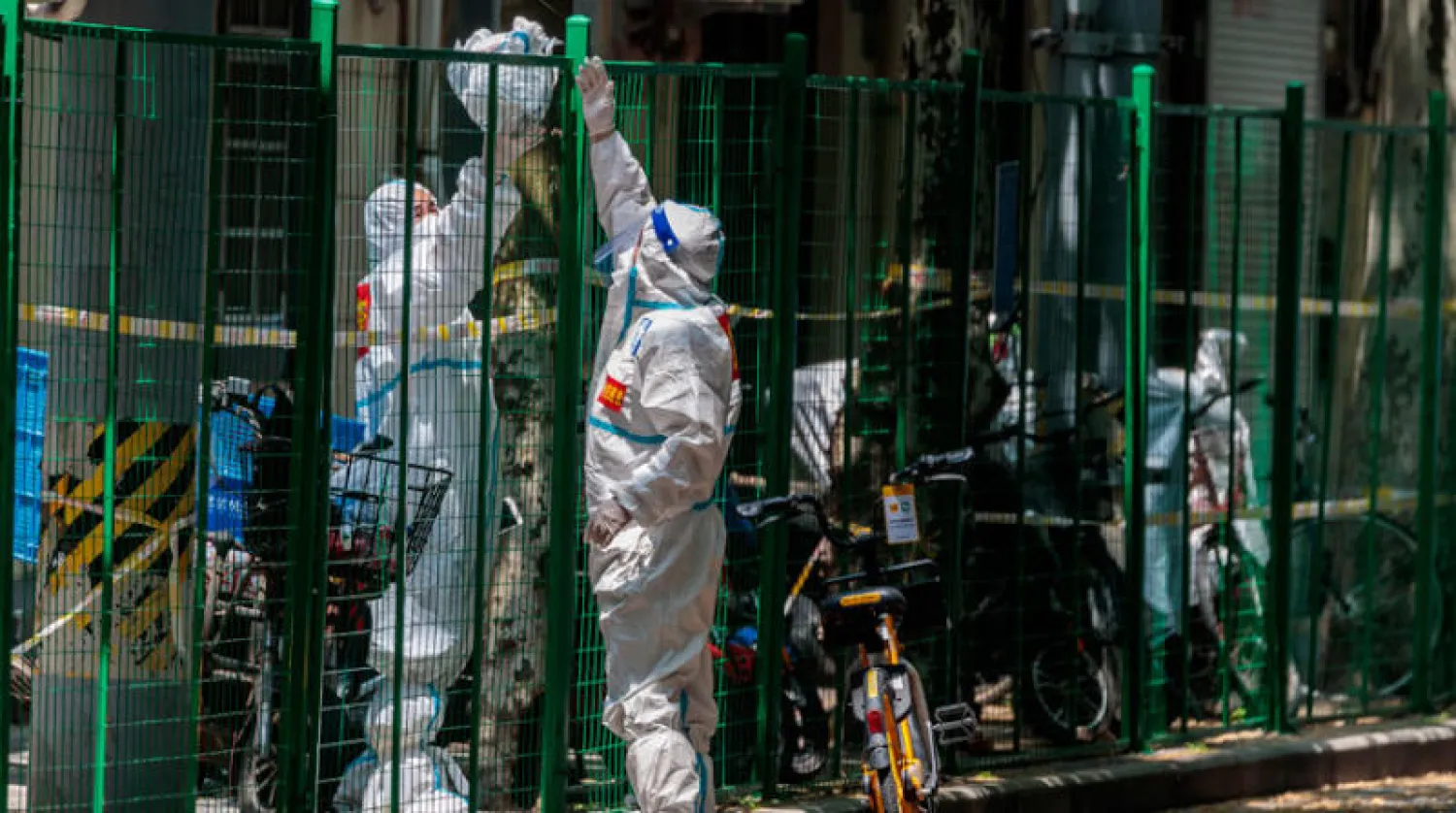 يتبادل أشخاص معدات الحماية فوق السياج في الشارع ، وسط إغلاق في شنغهاي أول من أمس (إ.ب.أ)