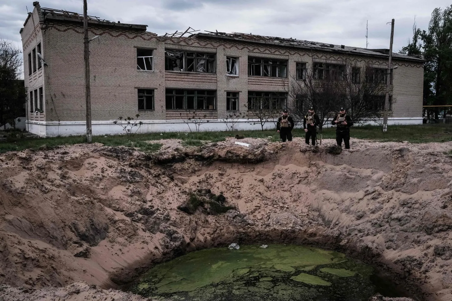 Three Ukrainian policemen stand at an explosion site past a destroyed school by shelling in Novomykolaivka, eastern Ukraine, on May 11, 2022, amid the Russian invasion of Ukraine. (AFP)