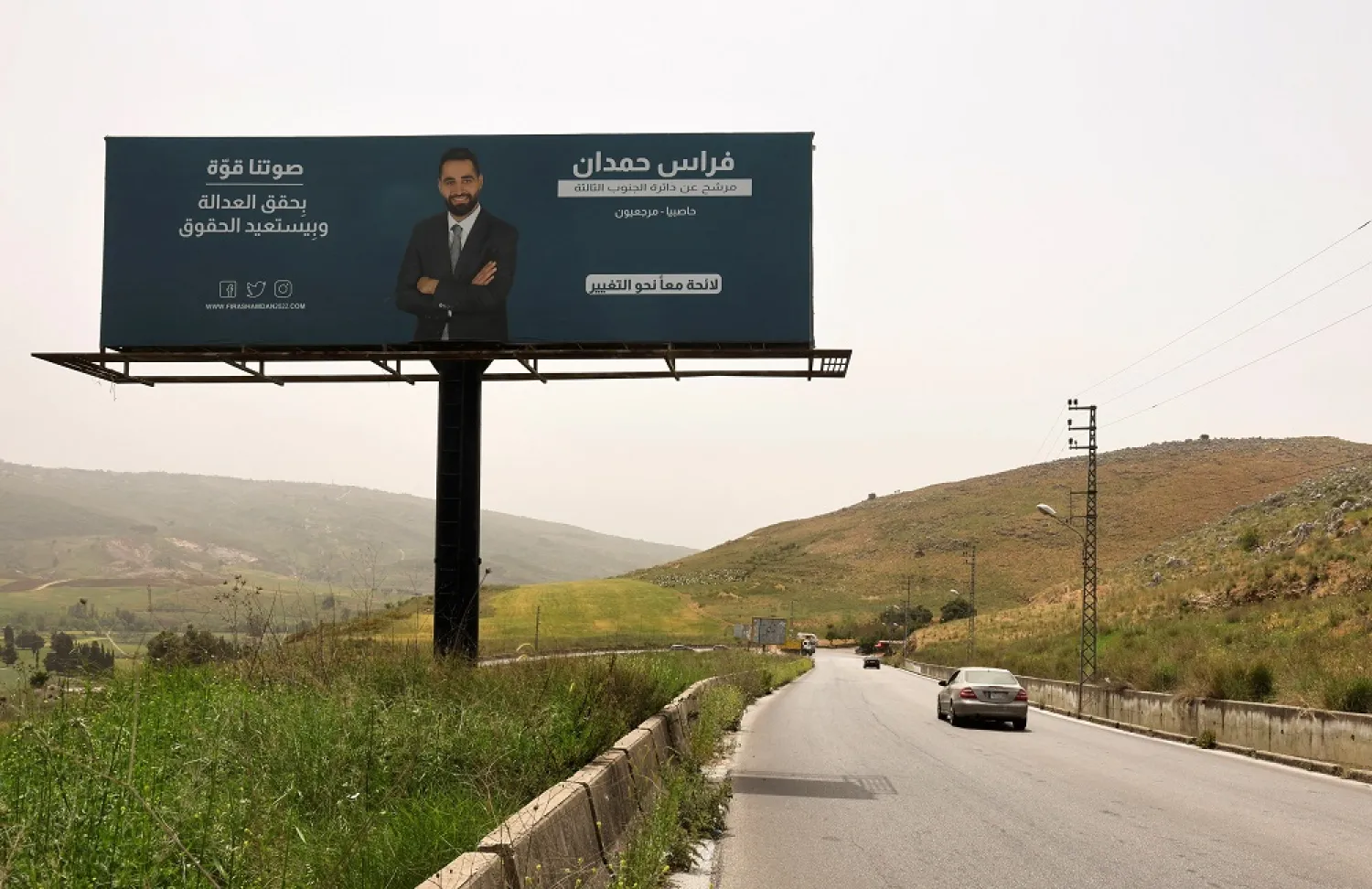 A car passes near an electoral campaign billboard depicting Firas Hamdan, a lawyer who is running as an opposition candidate in Lebanon's parliamentary election, in Kfar Tebnit village, southern Lebanon, April 30, 2022. Picture taken April 30, 2022. (Reuters)