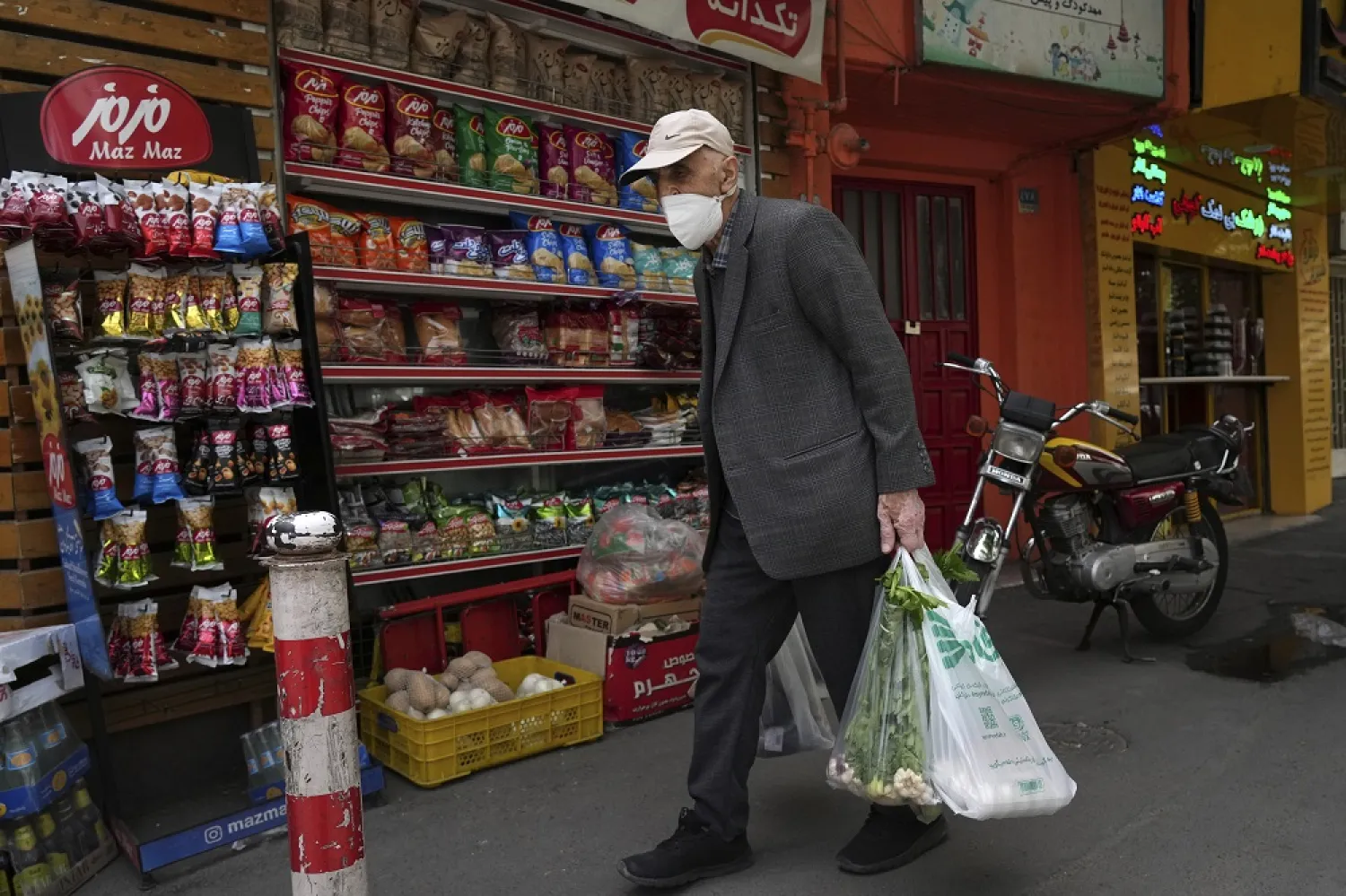 An elderly man carries his shopping in front of a grocery store in Tehran, Iran, Wednesday, May 11, 2022. (AP)