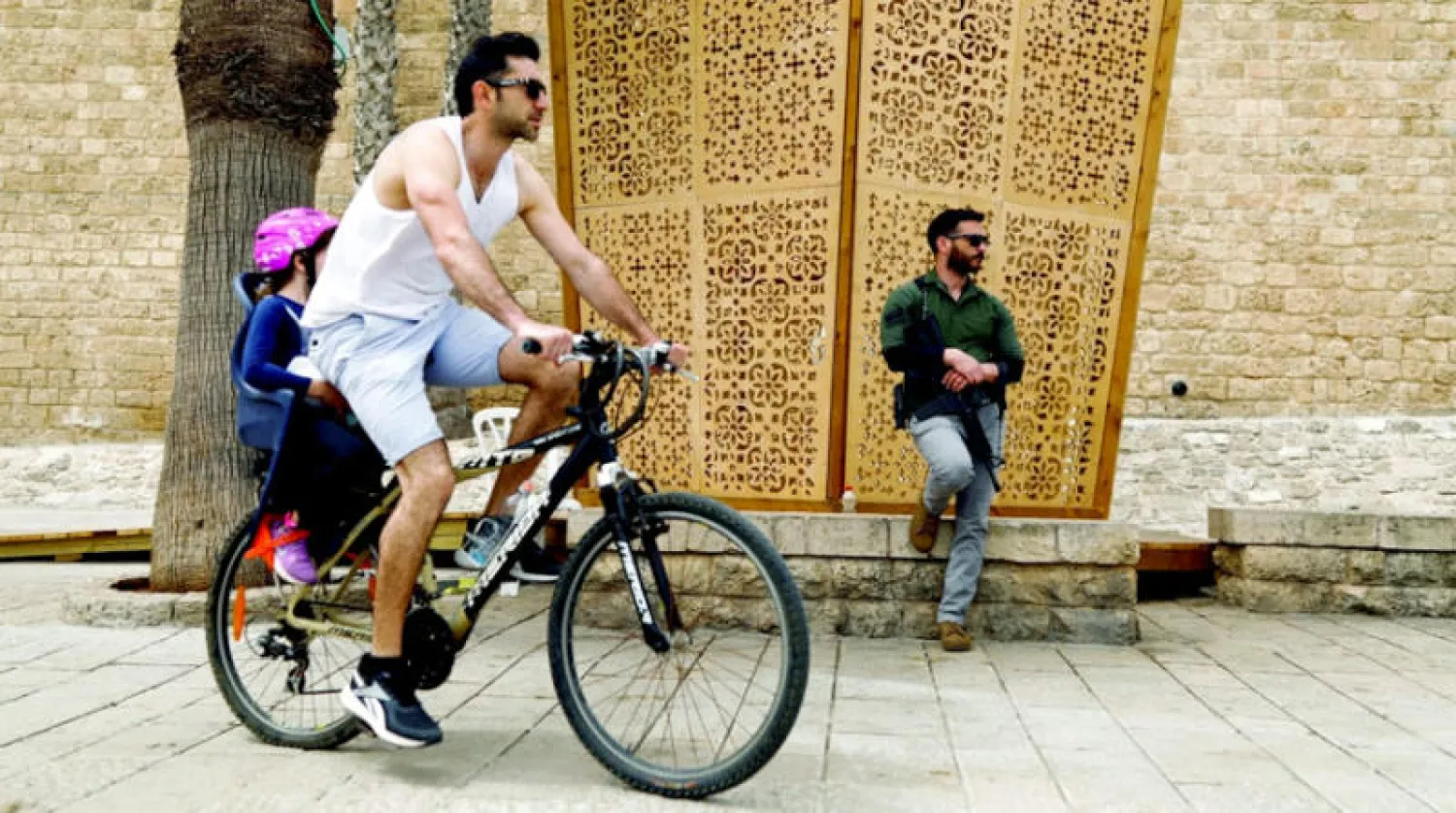 شاب يركب دراجة ويظهر مسؤول أمني إسرائيلي في شارع عام في يافا أبريل الماضي (رويترز)
