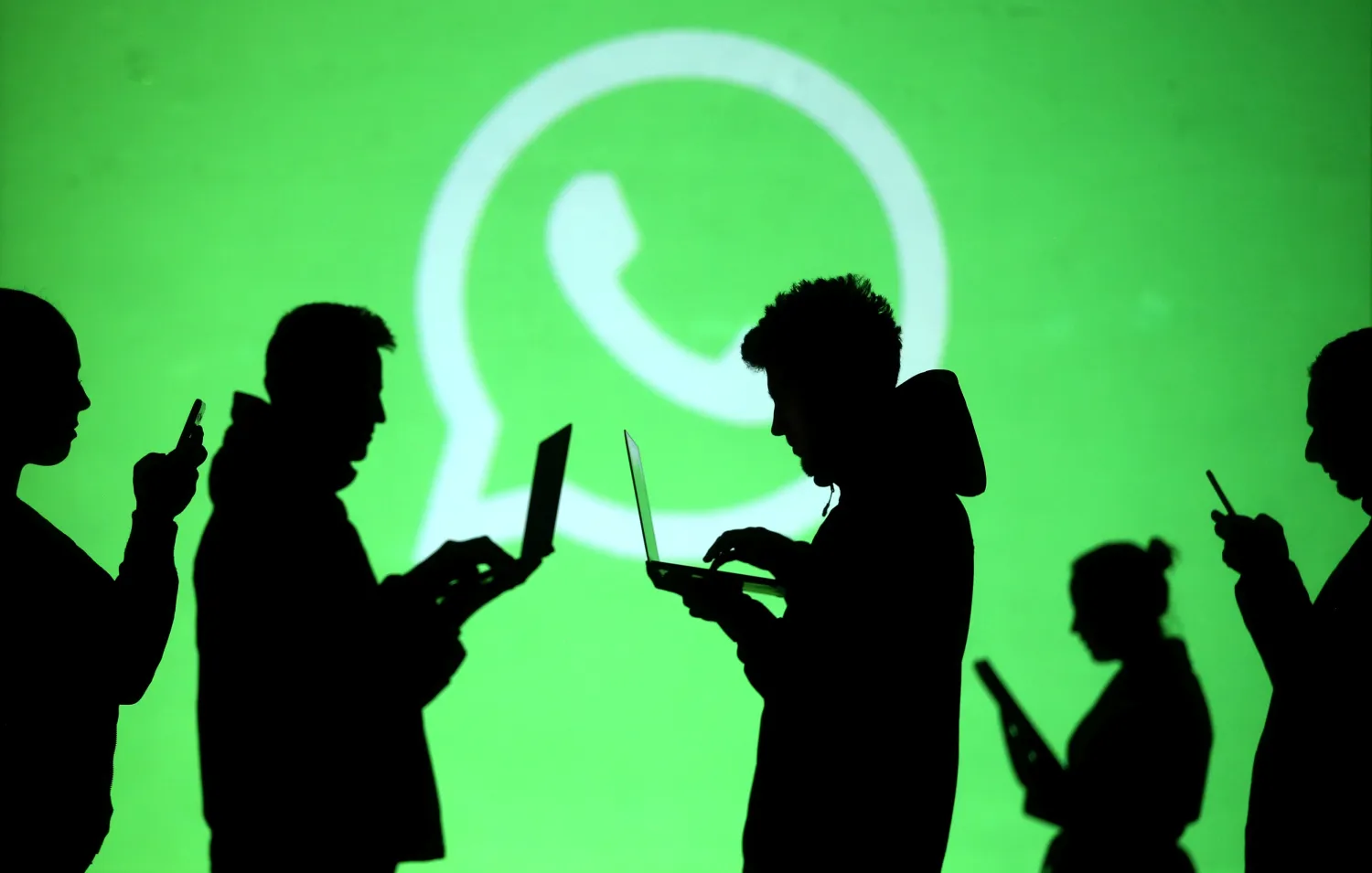 Silhouettes of laptop and mobile device users are seen next to a screen projection of Whatsapp logo in this picture illustration taken March 28, 2018. REUTERS/Dado Ruvic/Illustration/File Photo