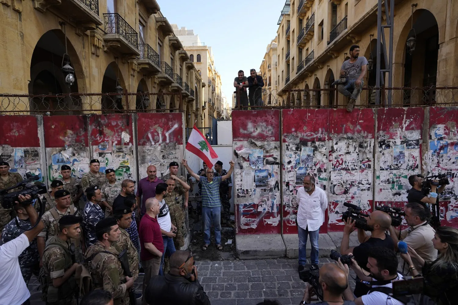 A Lebanese anti-government protester holds a national Lebanese flag as a team of engineers removes a concrete wall from a road that leads to the parliament building in Beirut, Lebanon, Monday, May 23, 2022. (AP)