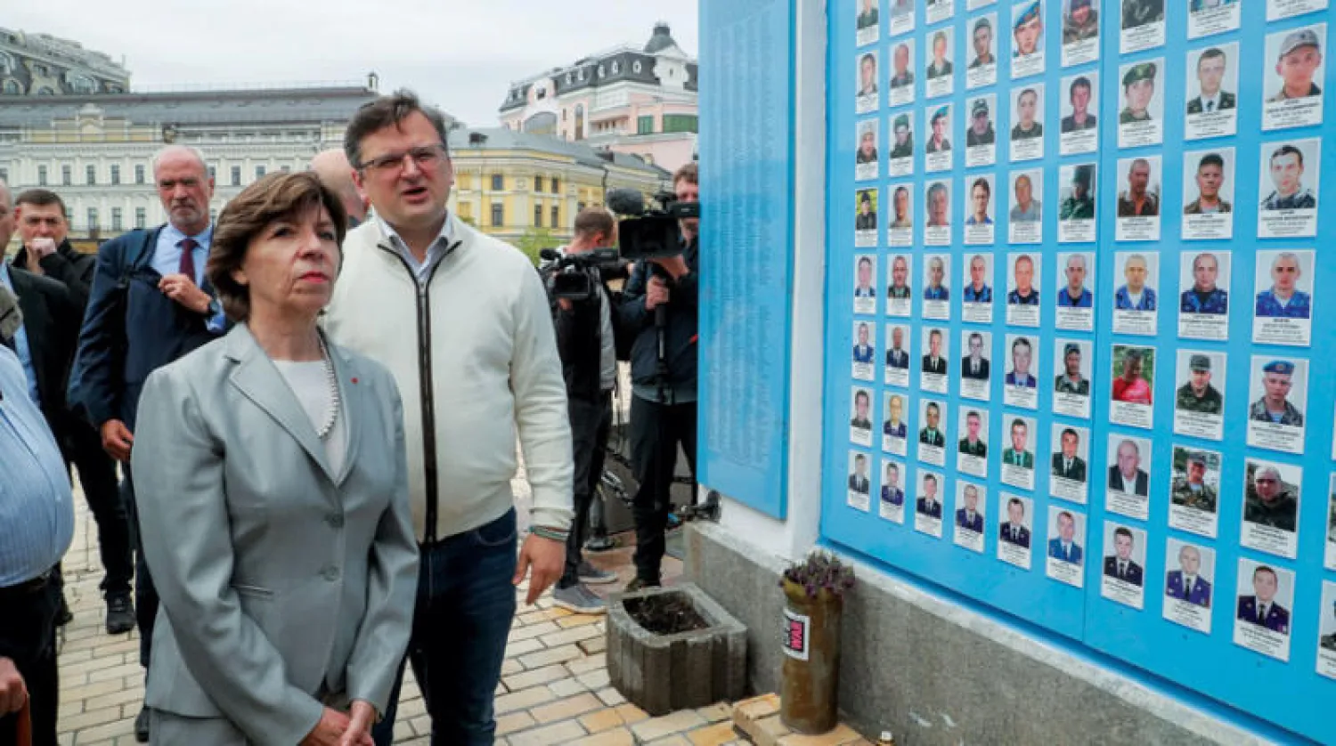 وزيرة الخارجية الفرنسية كاترين كولونا خلال زيارتها لجدار عليه صور قتلى أوكرانيين في كييف أمس (إ.ب.أ)