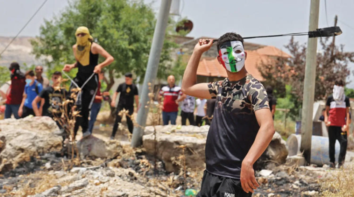 فلسطيني يرشق الحجارة وسط اشتباكات مع الأمن الإسرائيلي ومستوطنين في قرية عوريف في الضفة أمس (أ.ف.ب)