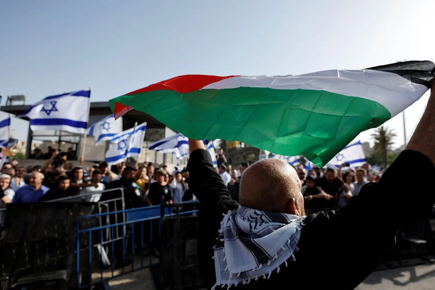 A Palestinian man holds up a Palestinian flag opposite to Israelis who hold Israeli flags by Damascus Gate to Jerusalem's Old City May 29, 2022. (Reuters)