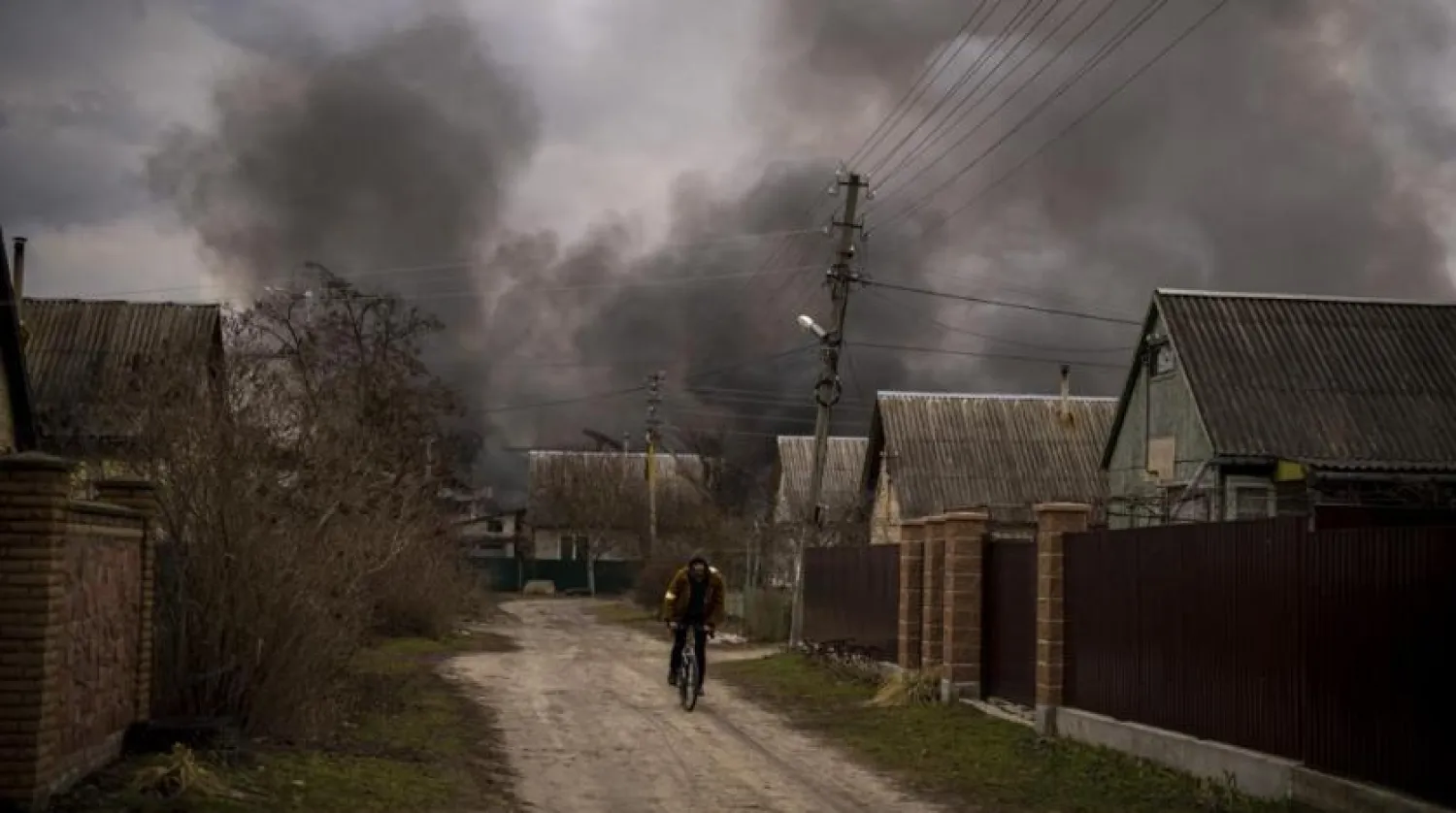 A Ukrainian man rides his bicycle near a factory and a store burning after it had been bombarded in Irpin, on the outskirts of Kyiv, Ukraine, Sunday, March 6, 2022. (AP)
