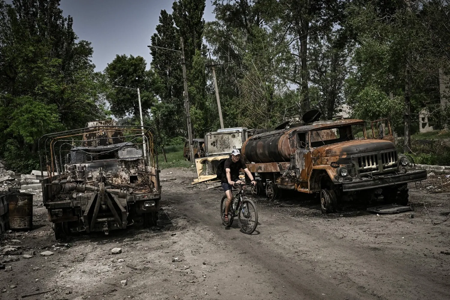 A man rides his bicycle between two destroyed military trucks in the city of Lysychansk, eastern Ukrainian region of Donbas, on June 11, 2022. (AFP) 