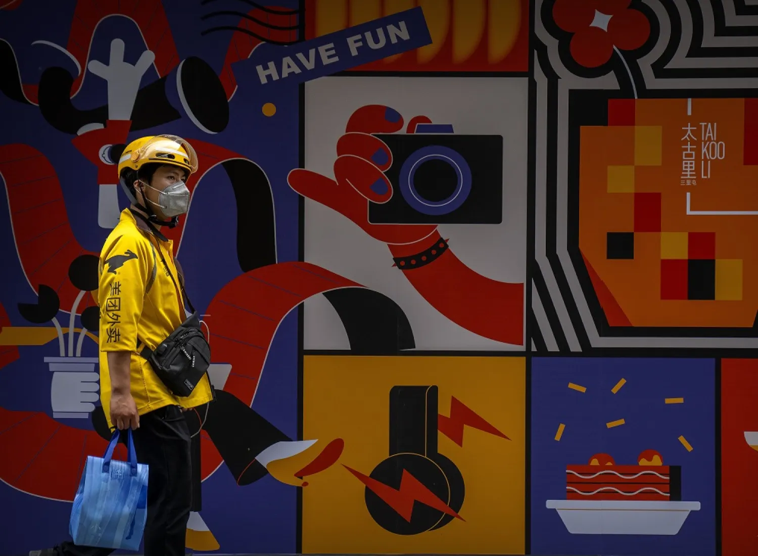 A delivery driver wearing a face mask walks past a mural at a shopping center in Beijing, Saturday, June 11, 2022. (AP) 