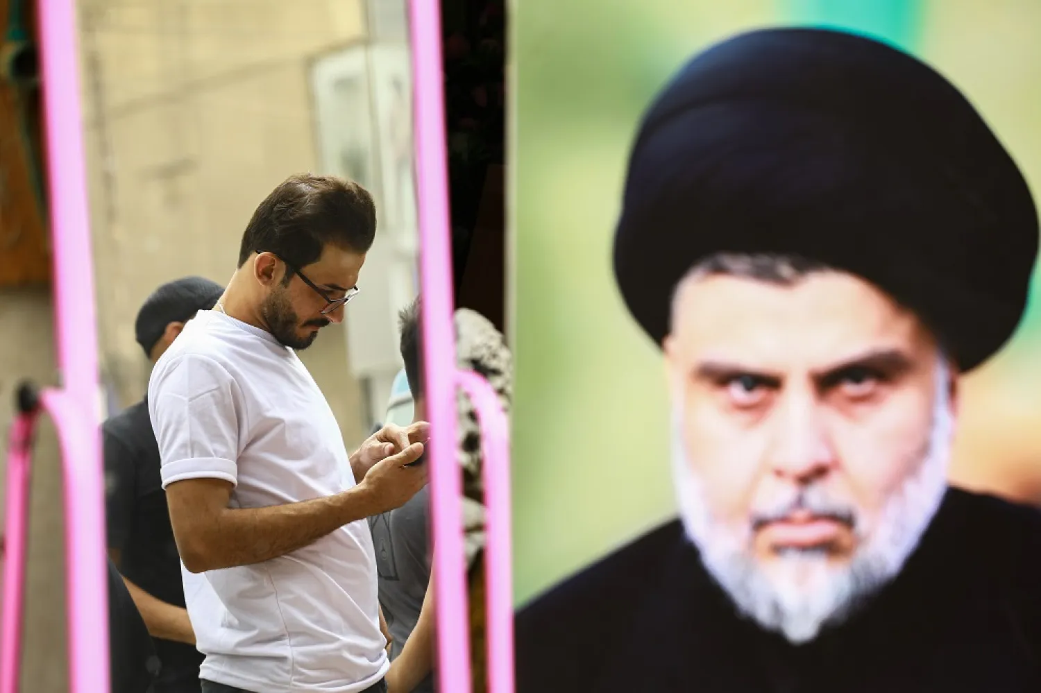 13 June 2022, Iraq, Sadr City: A man stands on the street near a poster bearing the picture of Iraqi Shiite cleric Moqtada al-Sadr. (dpa)