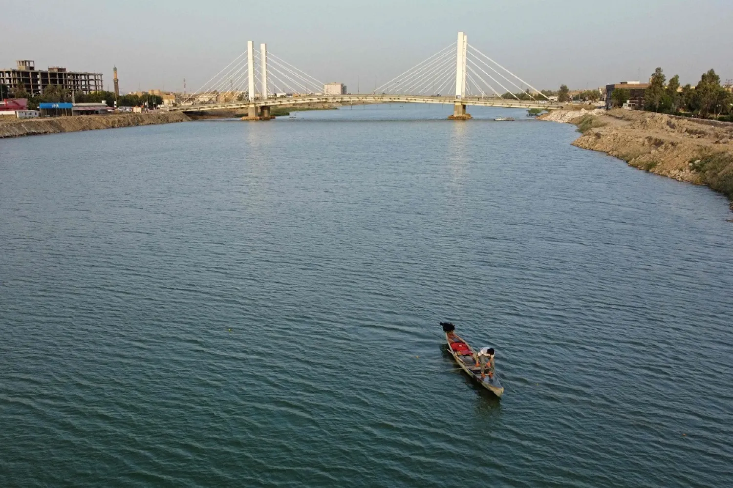 A fisherman casts a net in the Euphrates river near a pedestrian bridge in the city of Nasiriyah in Iraq's southern Dhi Qar province, on June 20, 2022. (Photo by Asaad NIAZI / AFP)