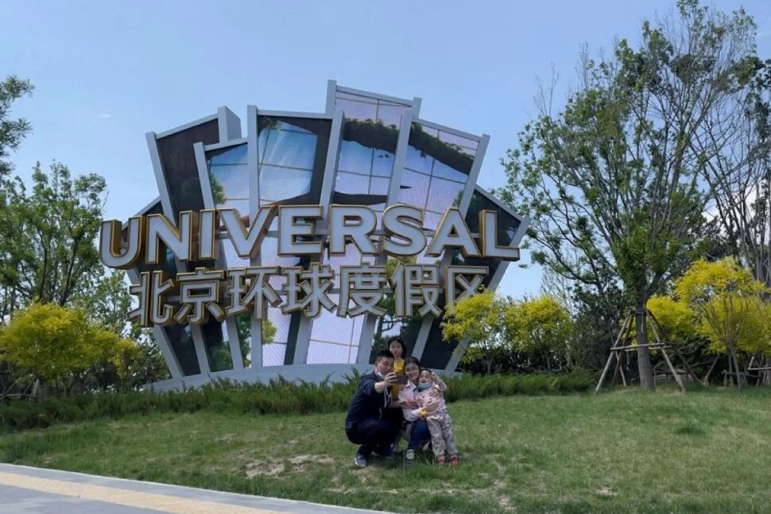 People pose in front of a sign of the Universal Beijing Resort, following its closure amid the coronavirus disease (COVID-19) outbreak, during the Labor Day holiday in Beijing, China May 1, 2022. (Reuters)