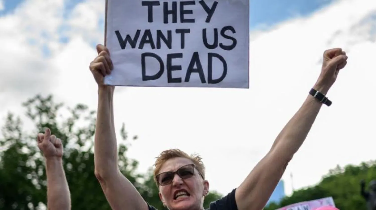 New York’taki bir protesto sırasında bir gösterici ‘Ölmemizi istiyorlar’ yazılı bir pankart tutuyor (AFP)