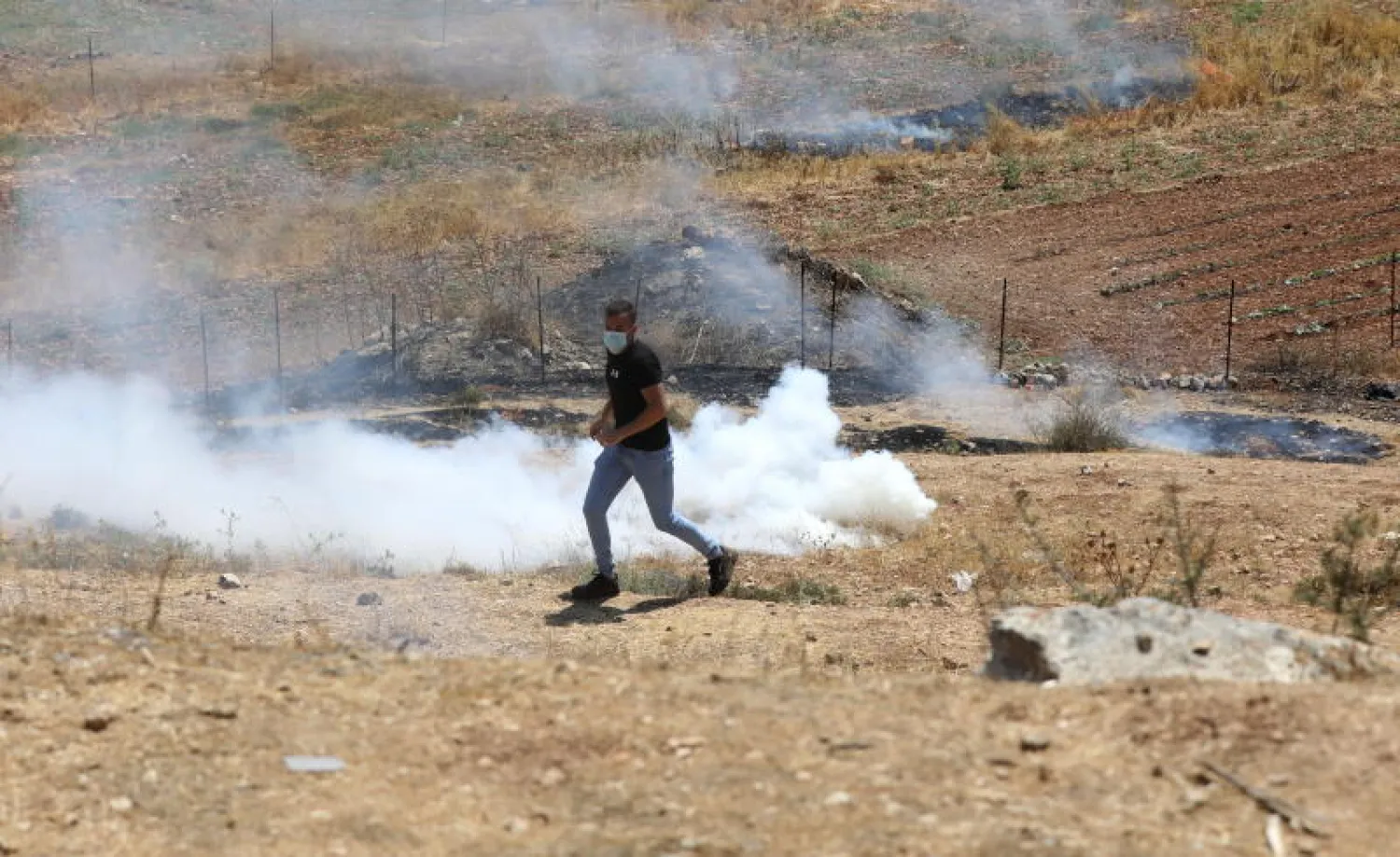متظاهر فلسطيني يركض هرباً من القنابل المسيلة للدموع خلال اشتباكات مع الجيش الإسرائيلي في الضفة الغربية (إ.ب.أ)