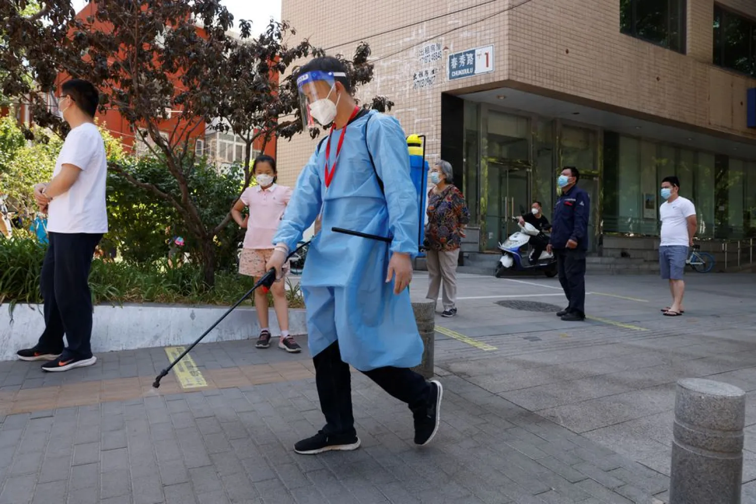 A worker wearing personal protective equipment (PPE) sprays disinfectant next to people lining up to get tested at a makeshift nucleic acid testing site amid the coronavirus disease (COVID-19) outbreak in Beijing, China May 27, 2022. REUTERS/Carlos Garcia Rawlins