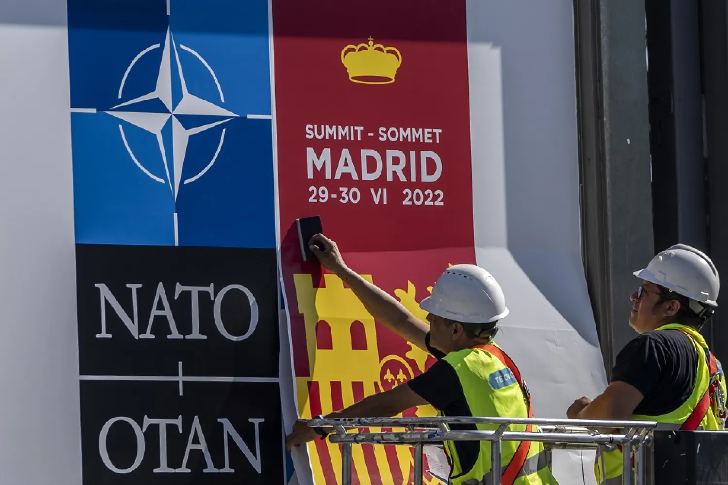 A worker fixes a NATO poster outside the NATO Summit building ahead of the summit in Madrid, Spain, Monday, June 27, 2022. (AP)
