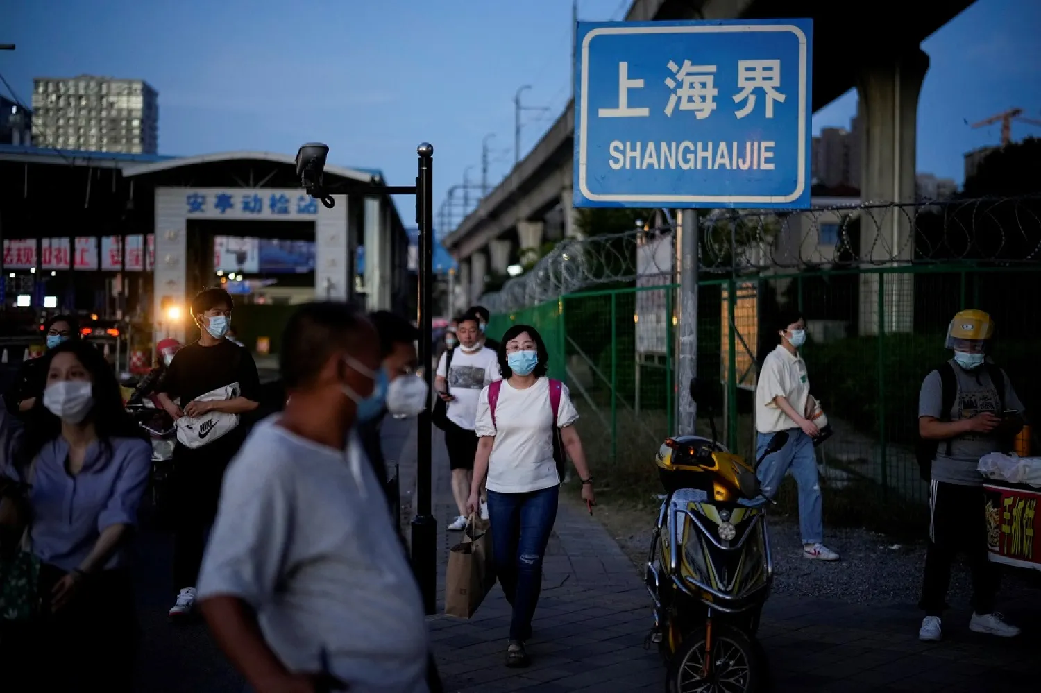 People, wearing a face mask following the coronavirus disease (COVID-19) outbreak, walk past a barrier on a street on a border between Shanghai and Jiangsu Province in Shanghai, China July 1, 2022. (Reuters)