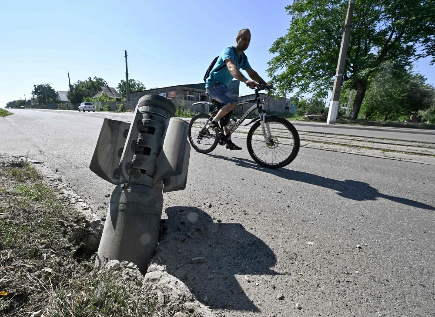 A cyclist rides past a tail section of a rocket embedded in a road in Kramatorsk on July 4, 2022, the day after a Russian rocket attack. (AFP) 