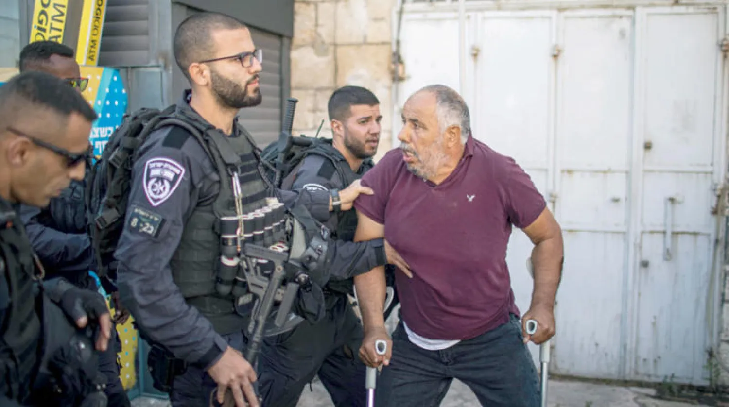 شرطي إسرائيلي يحاول إبعاد فلسطيني بعكازين خلال احتجاجات في القدس الشرقية أمس (د.ب.أ)
