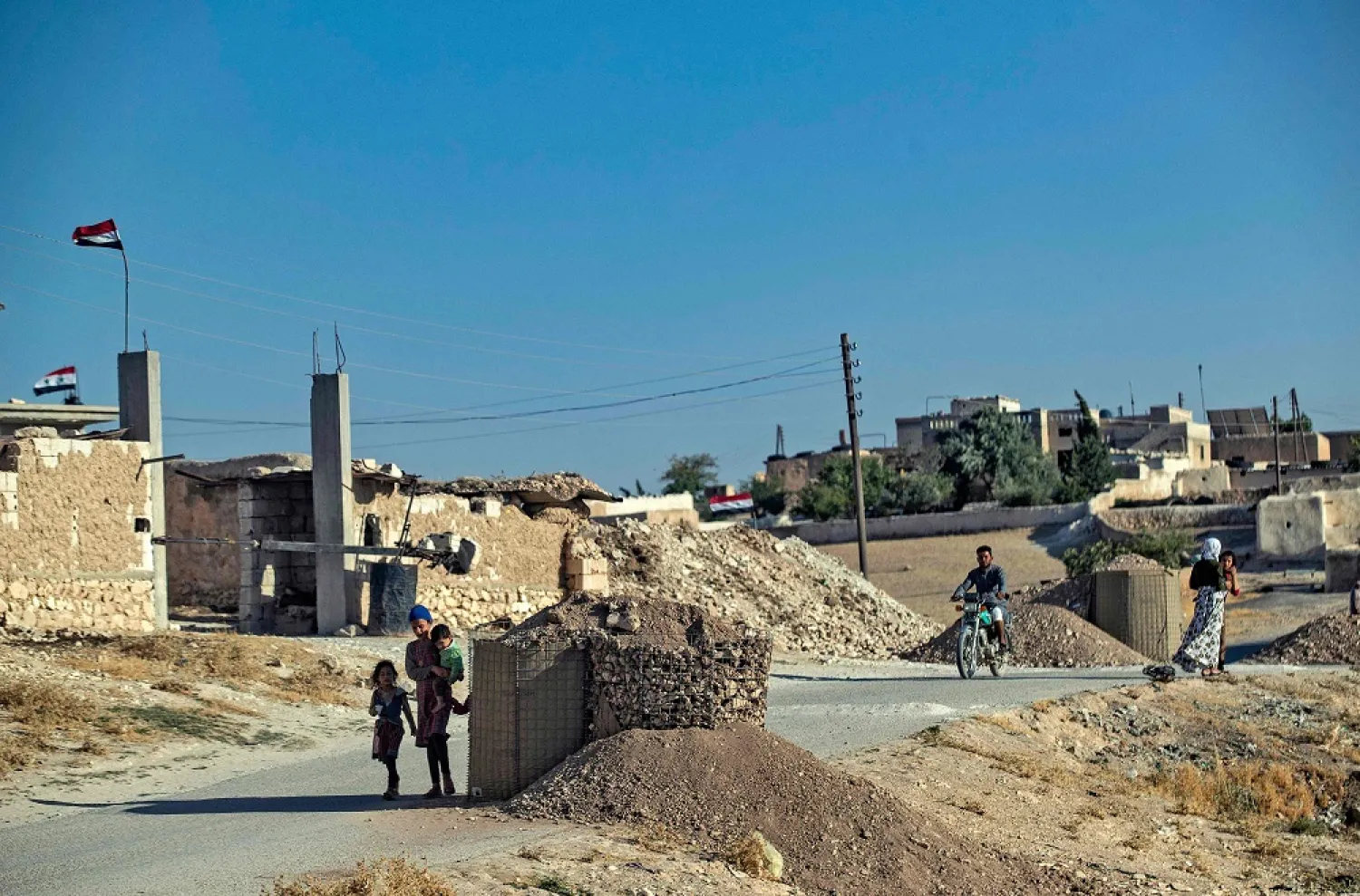 Civilians walk near Syrian government forces stationed on the front line in the countryside of Syria's northern city of Manbij, located near the border with Turkey, on July 21, 2022. (AFP)