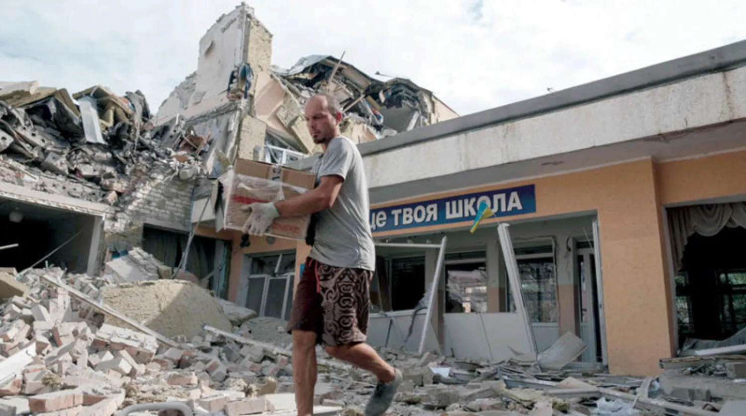 مدرس ينقل أغراضاً بعد قصف مدرسة في قرية بإقليم دونيتسك الأحد (أ.ف.ب)