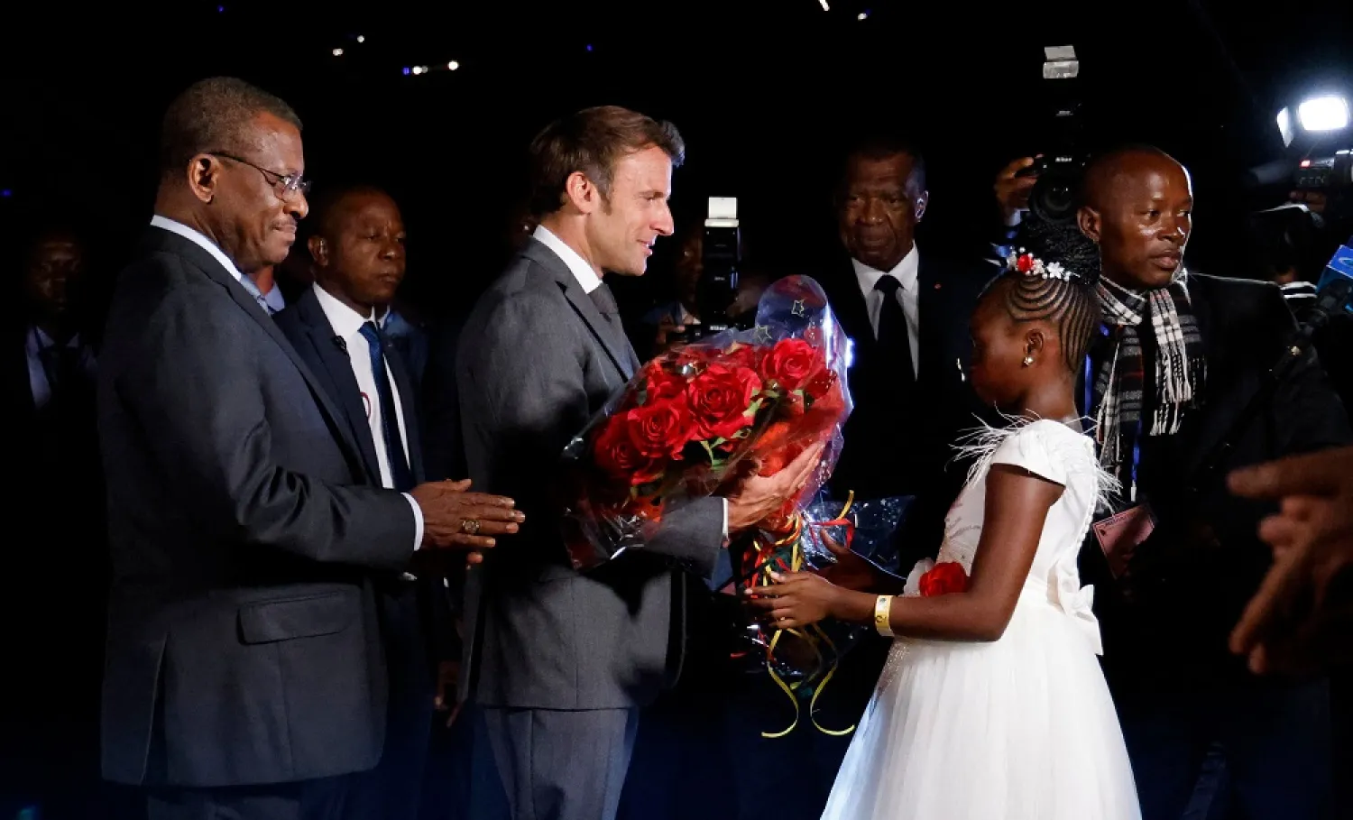 A young girl gives flowers to French president Emmanuel Macron as he is welcomed by Cameroonese Prime Minister Joseph Dion Ngute (L) at the airport on July 25, 2022, in Yaounde. (AFP)
