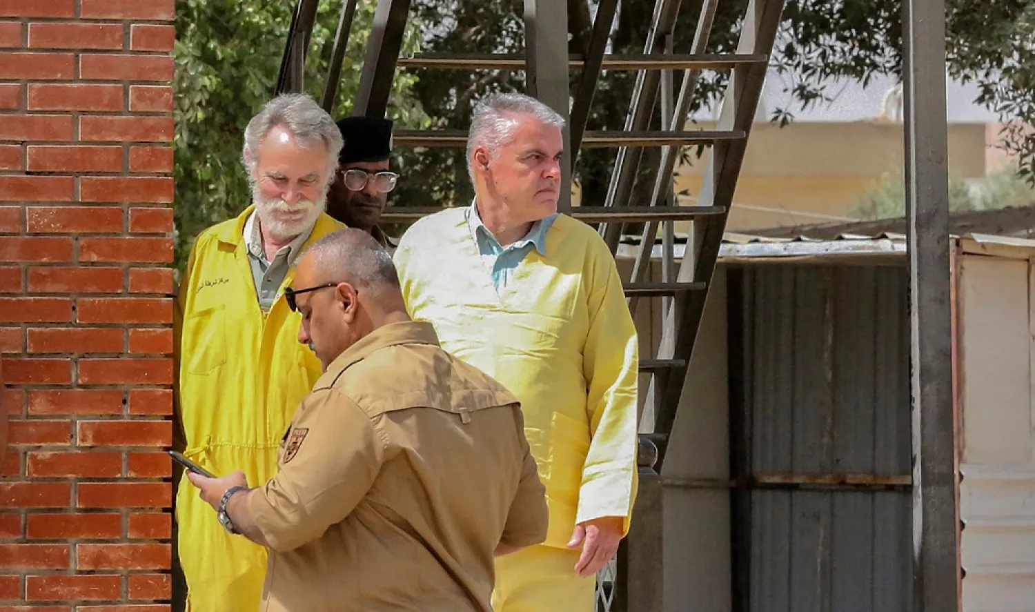 In this file photo taken on May 22, 2022 James Fitton, 66, a retired British geologist (L) and Volker Waldmann, 60, a Berlin psychologist, are dressed in the yellow uniform of detainees as they are arrive at a courthouse in the Iraqi capital Baghdad, where they are being tried over ancient pottery shards, considered by the Iraqi authorities as antiquities, found in their luggage at the airport. (AFP)