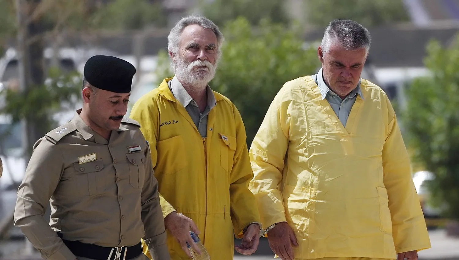 Volker Waldmann, right, and Jim Fitton, center, are handcuffed as they walk to a courtroom escorted by police arriving to court in Baghdad, Iraq, Sunday, May 22, 2022. (AP)