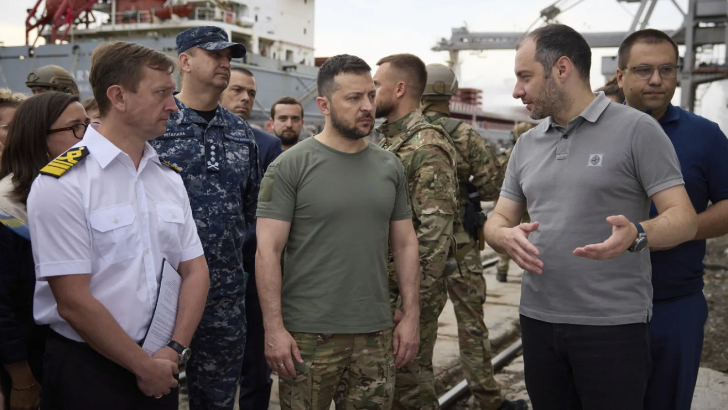 Ukrainian President Volodymyr Zelenskyy, center, surrounded by ambassadors of different countries, UN and other officials, visits a port during loading of grain on a Turkish ship, background, in Odesa region, Ukraine, Friday, July 29, 2022. Ukrainian Presidential Press Office via AP/TASS