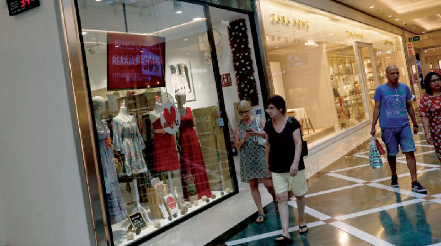 أشخاص يسيرون بالقرب من مقياس حرارة يعرض درجة 26.8 درجة مئوية في مركز تسوق بمدريد (رويترز)