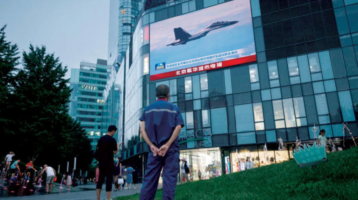 رجل يشاهد طائرة مقاتلة خلال مناورات صينية قرب تايوان على شاشة في بكين أمس (رويترز)