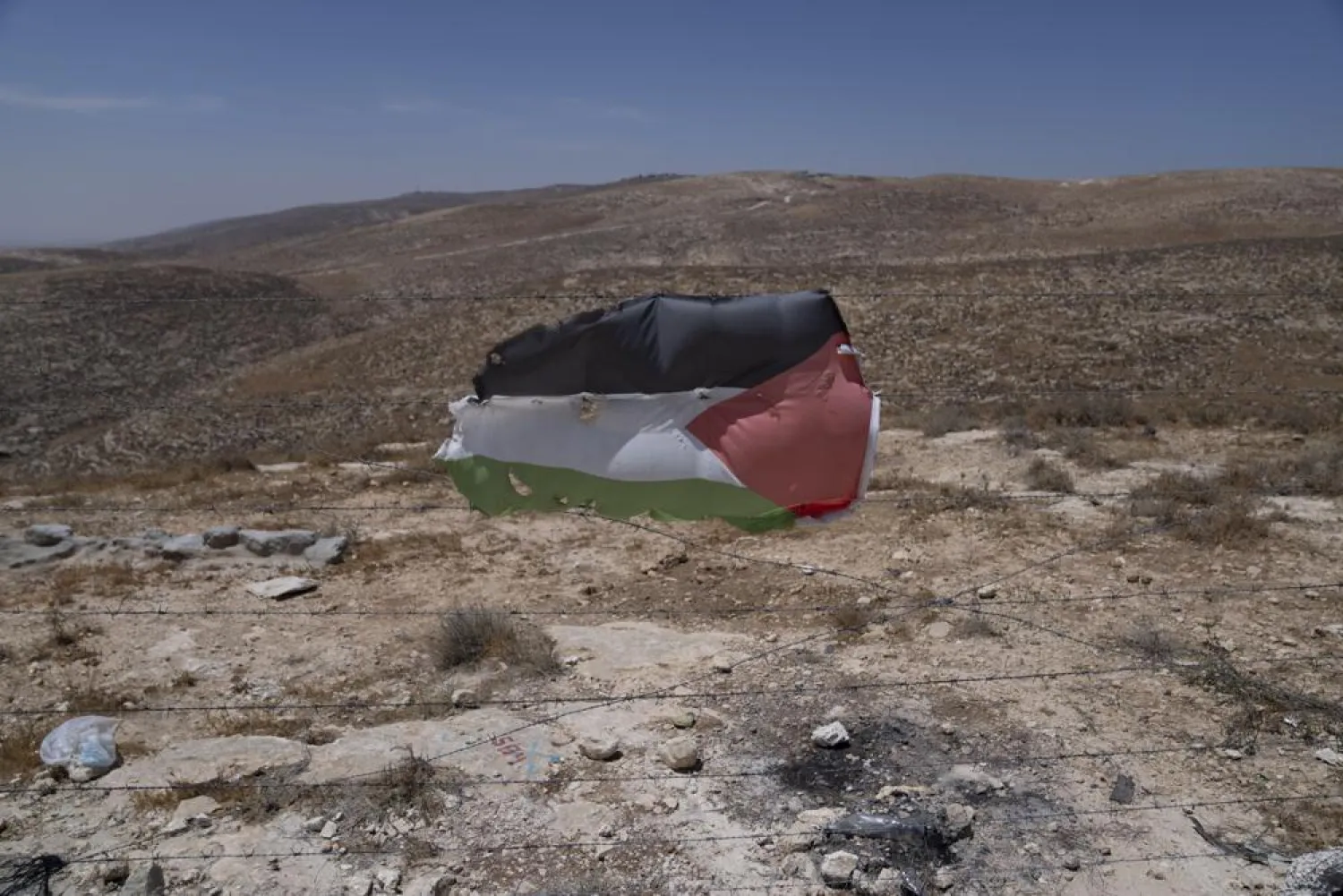 A Palestinian flag is posted at a barbed wired at the Palestinian hamlet of Khallat al-Dhaba, in the cluster of Bedouin communities in Masafer Yatta, West Bank, Monday, Aug. 1, 2022. (AP Photo/Nasser Nasser)
