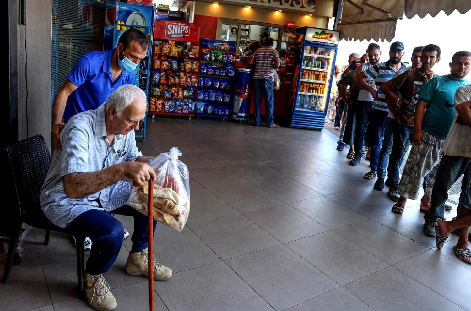An elderly man rests outside after buying a bag of subsidized flatbread, as others continue to wait in a queue, in the Lebanese capital Beirut on July 29, 2022, amid a shortage of wheat supplies. (AFP)