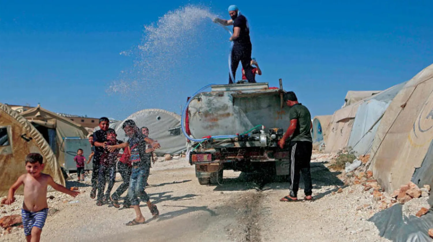 متطوعون يرشون الأطفال بالماء وسط درجات الحرارة المرتفعة في مخيم للنازحين السوريين قرب قرية كيلي على الحدود التركية (أ.ف.ب)