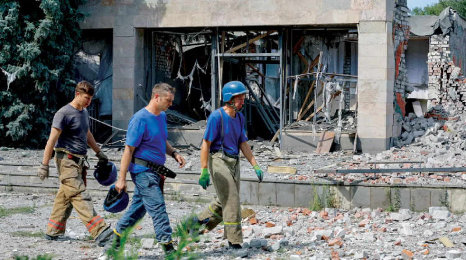 عناصر من الدفاع المدني يمرون أمام بناية دمرها القصف في بلدة بمنطقة دونيتسك الاثنين (رويترز)