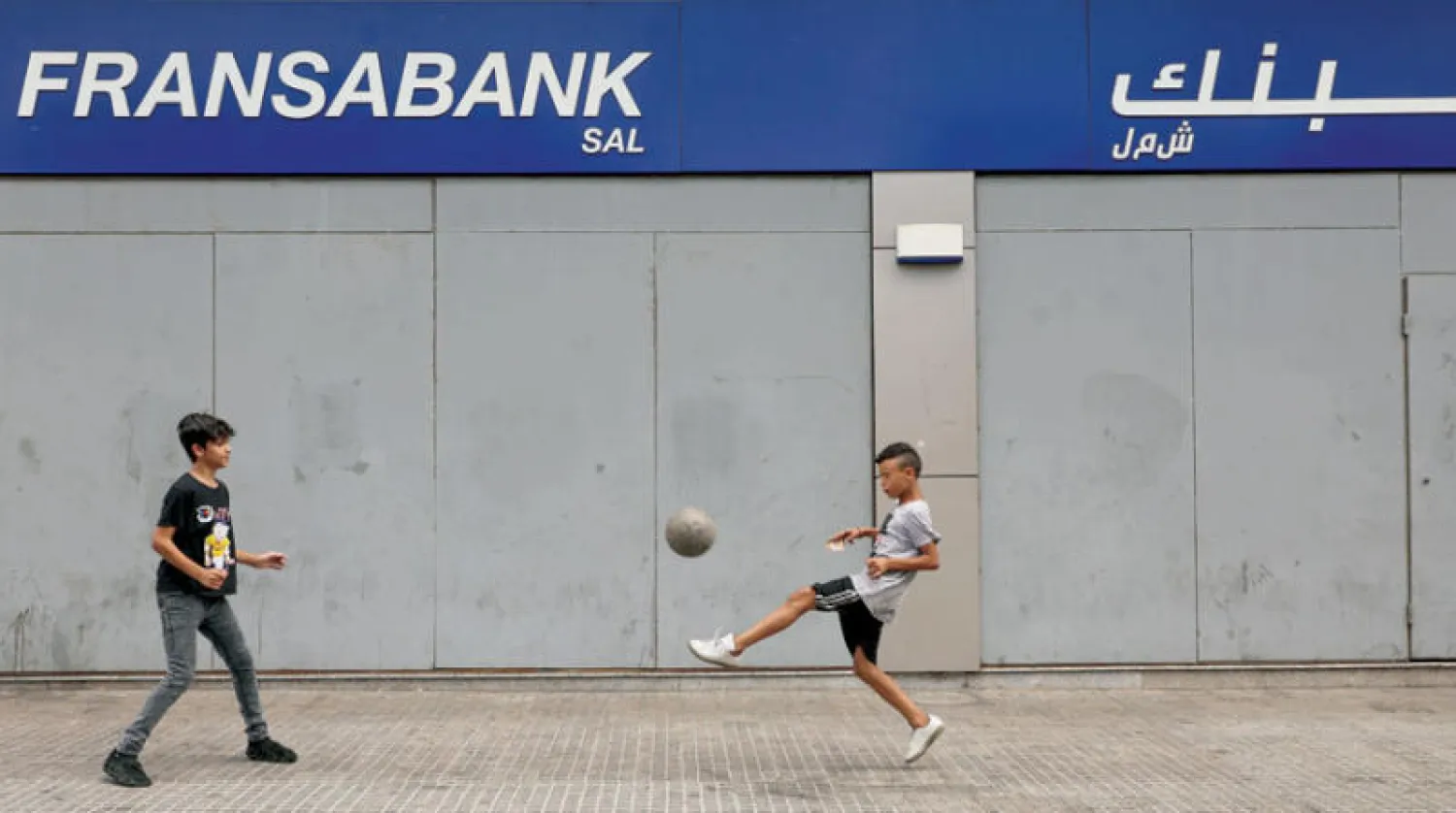 أولاد يلعبون بكرة القدم أمام فرع أحد البنوك المغلقة بسبب الإضراب في بيروت أمس (رويترز)