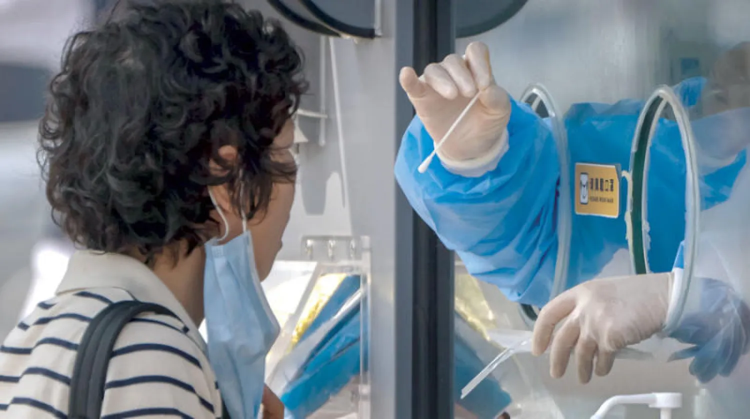 امرأة تستعد لمسح حلقها في مركز اختبار فيروس «كورونا» في بكين الجمعة (أ.ب)