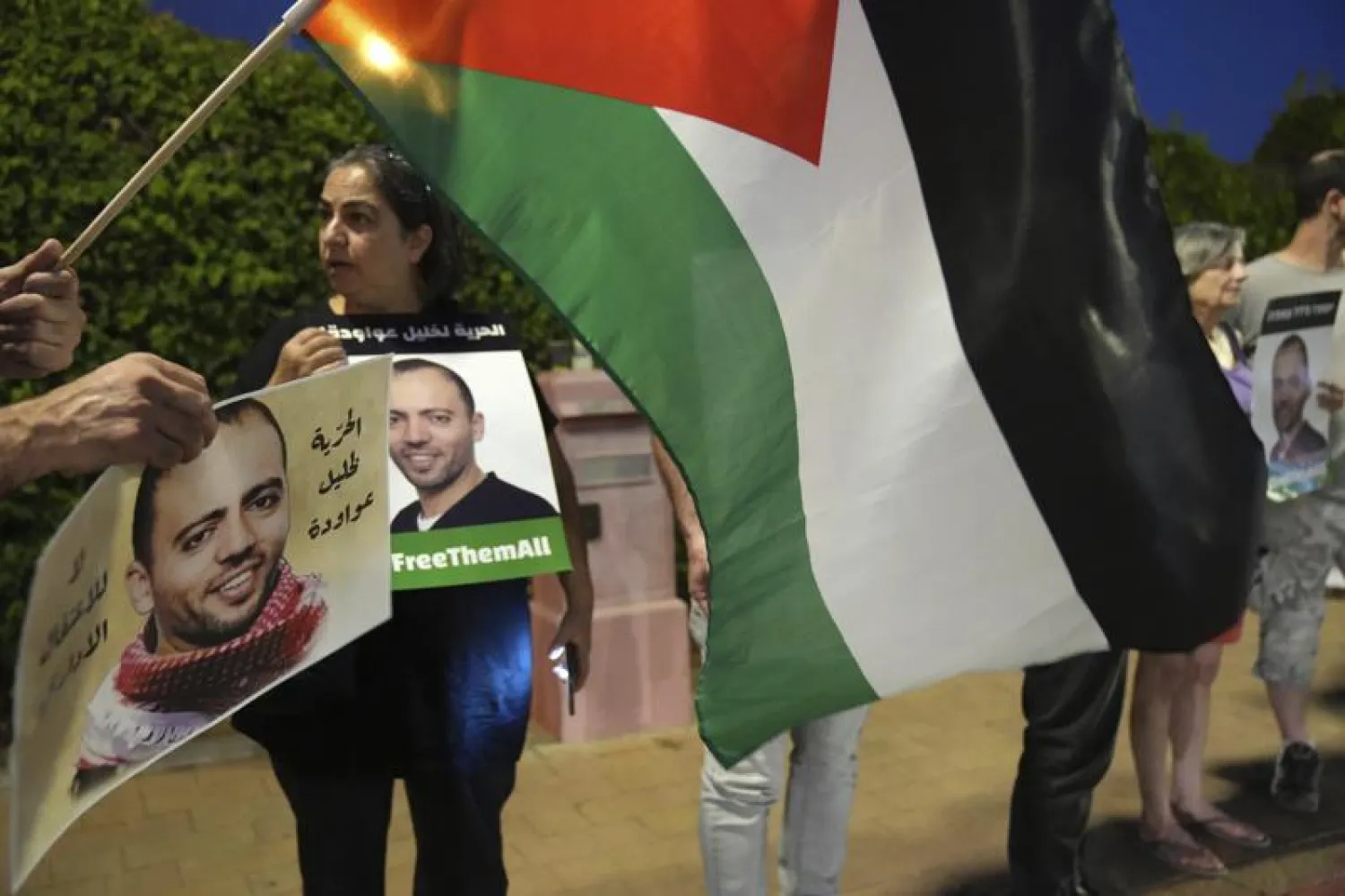 Protesters gather with a Palestinian flag outside the hospital where Palestinian Khalil Awawdeh, pictured in the placards, a prisoner in Israel on hunger strike, is now clinging to life in Be'er Yaakov, Saturday, Aug. 13, 2022. Arabic on the placard reads, "Freedom for Khalil Awawdeh."  (AP Photo/Tsafrir Abayov)
