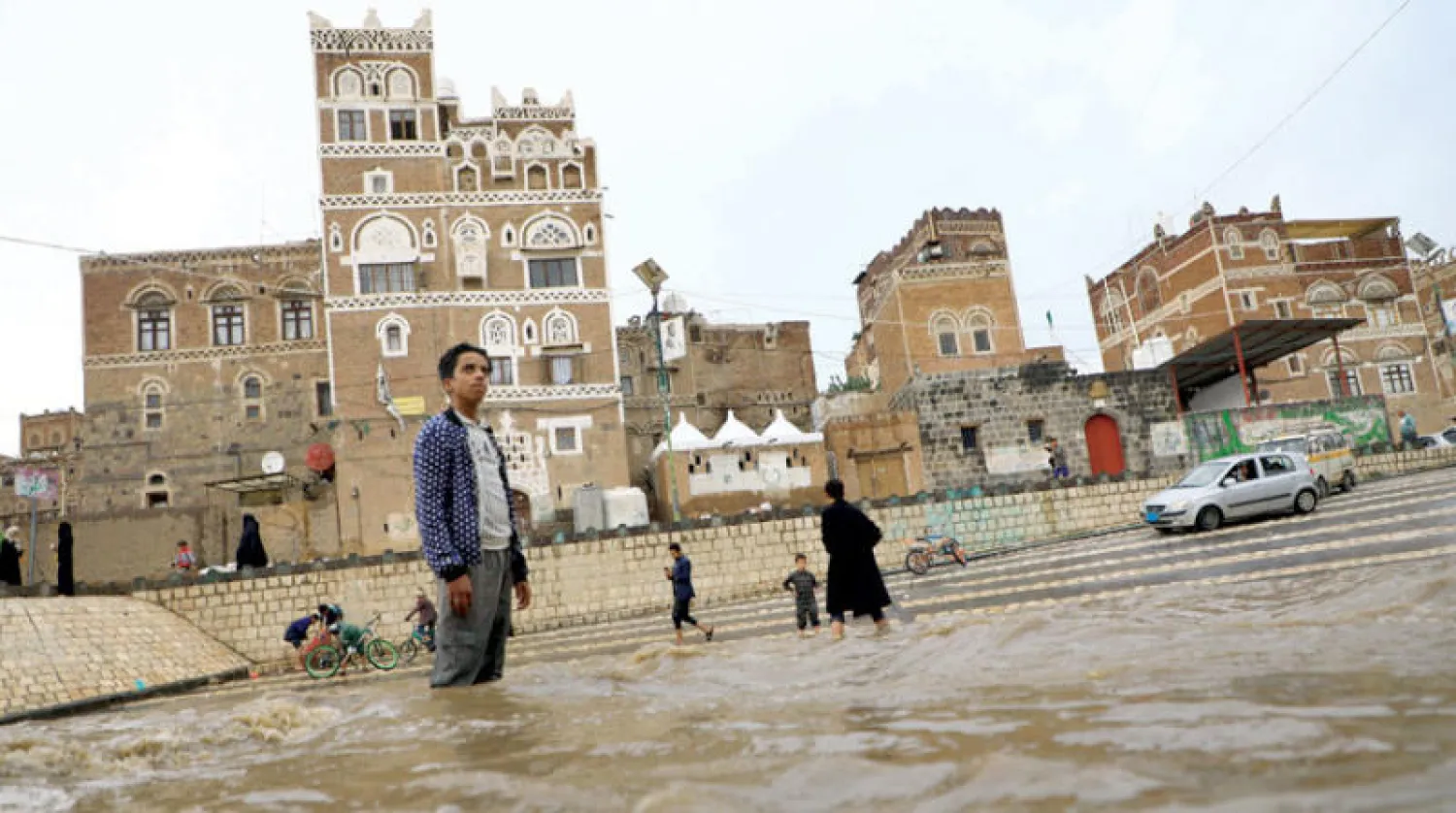 يمنيون يعبرون أحد الشوارع التي غمرتها مياه الأمطار الغزيرة في صنعاء (أ.ف.ب)