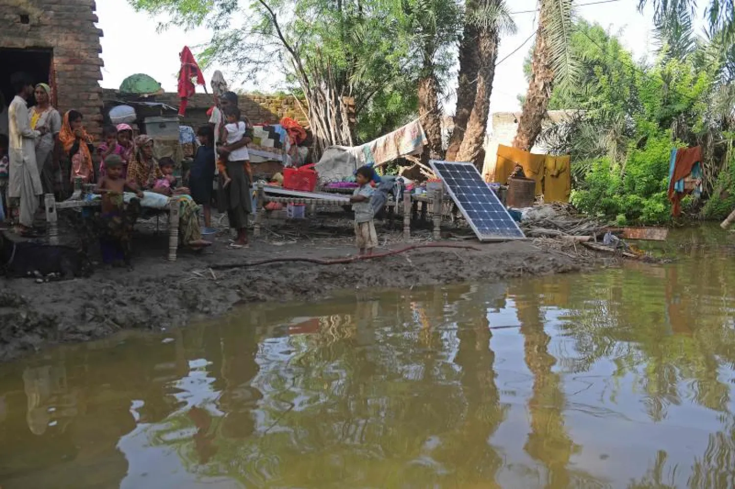 أسرة تجلس أمام منزلها الطيني الذي دمرته الفيضانات في ضواحي سكور بإقليم السند (أ.ف.ب)