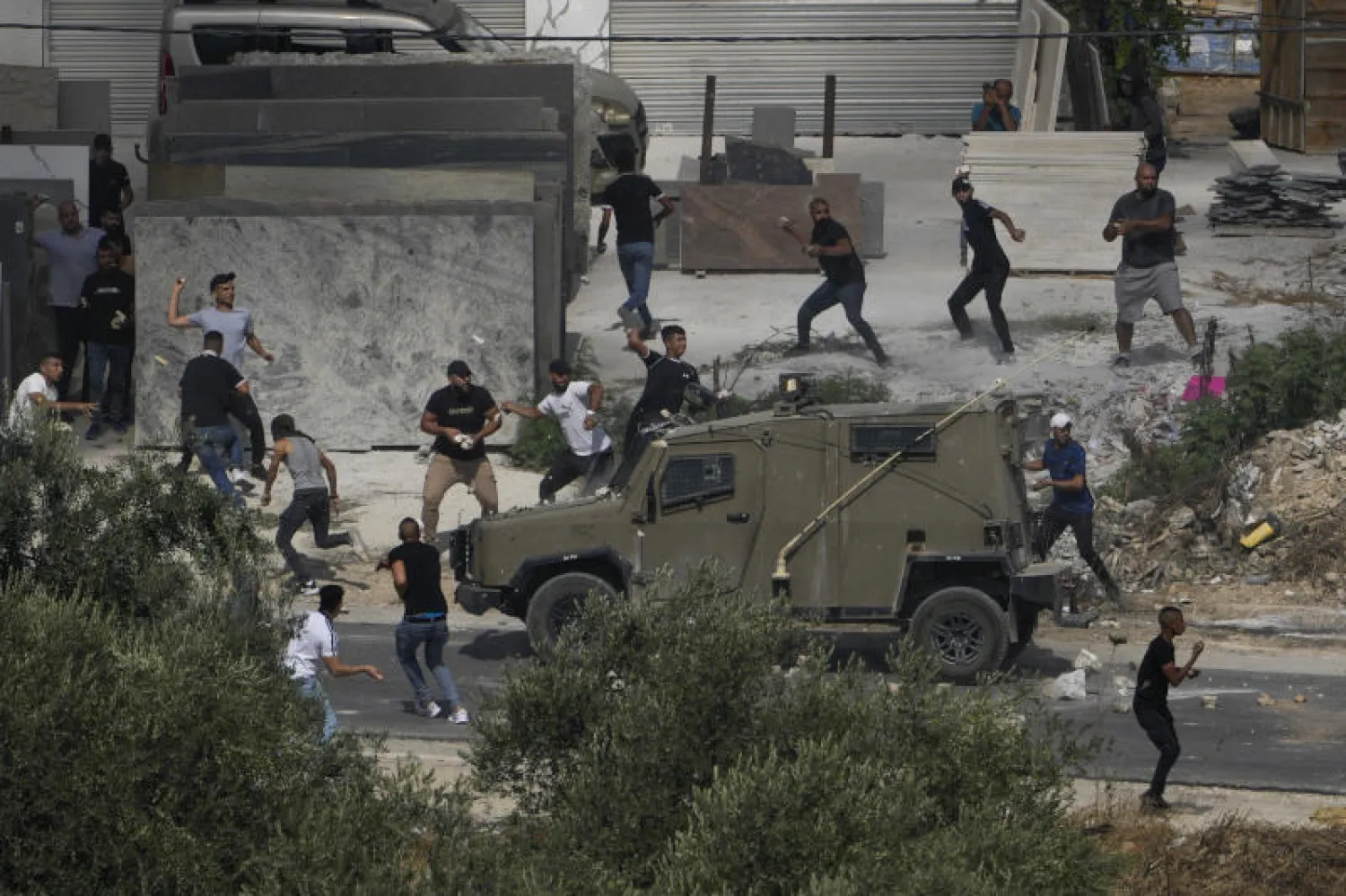 فلسطينيون يرشقون مركبات عسكرية بالحجارة خلال عملية إسرائيلية في قرية رجب بالضفة الثلاثاء (أ.ب)