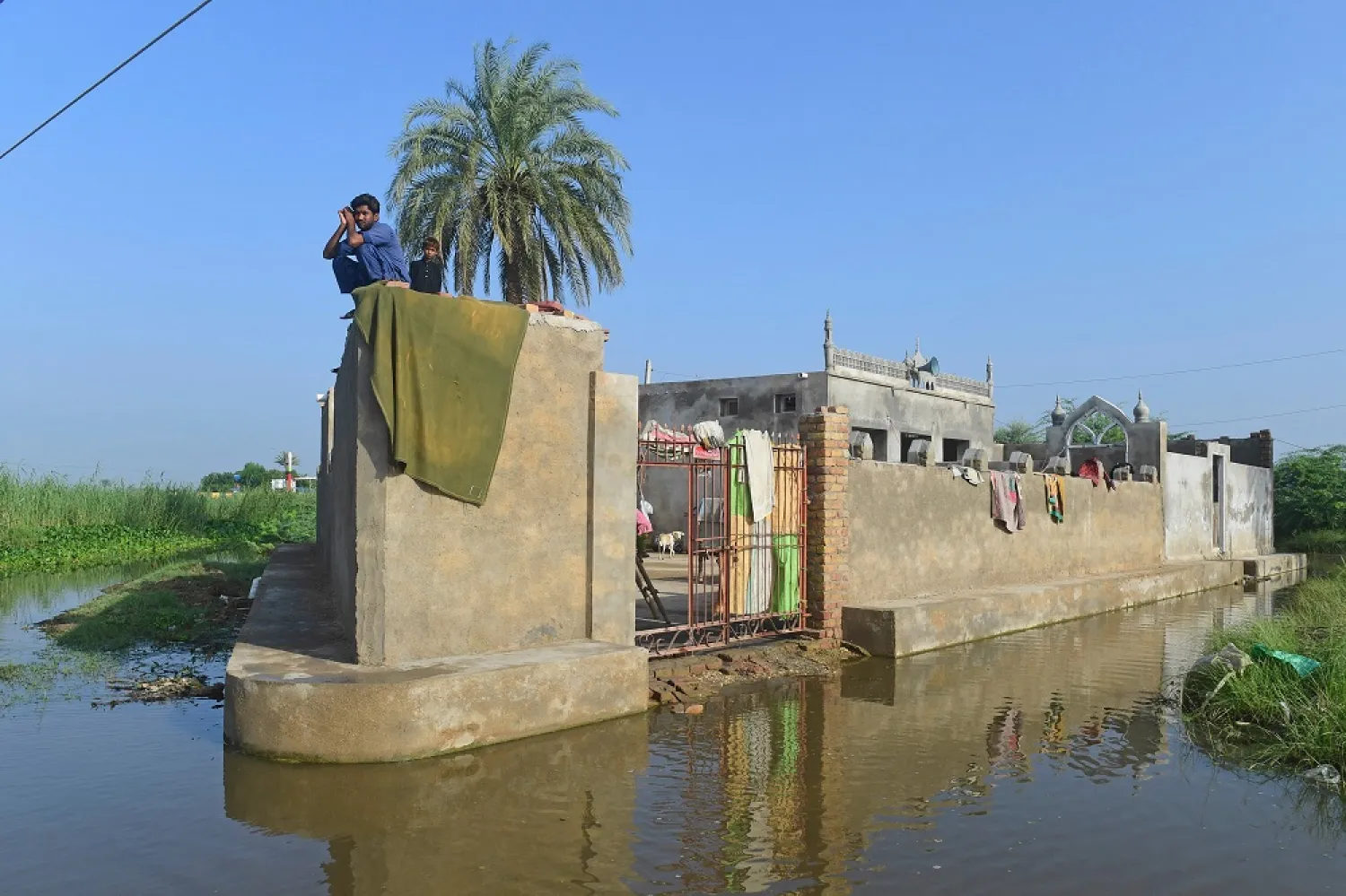 A flood-affected man along with a boy sits atop their house in flood-hit Sukkur, Sindh province on September 2, 2022. (AFP)