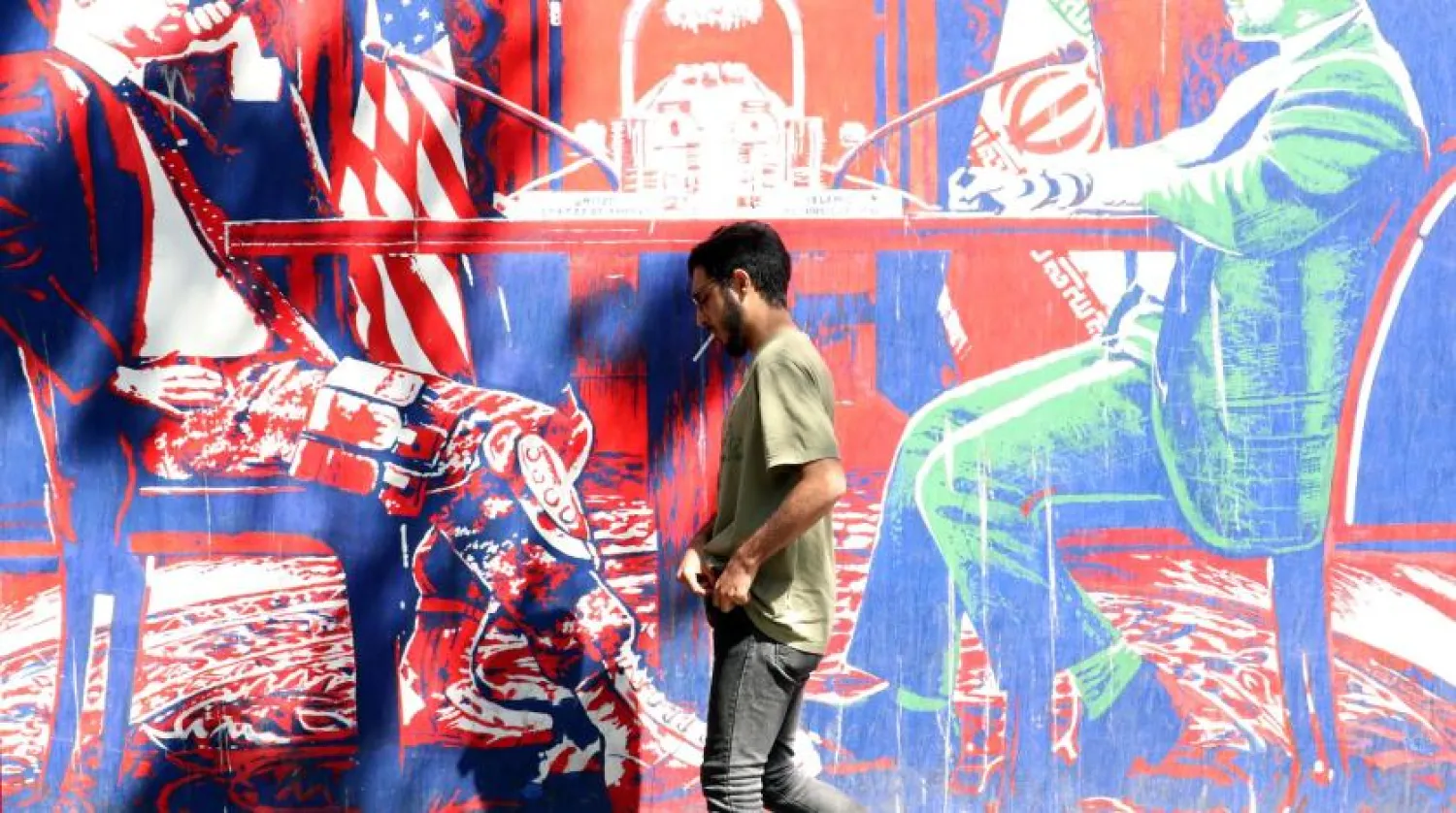  An Iranian man walks next to mural depicting the negotiating table on the wall of the former US embassy in Tehran (EPA).

