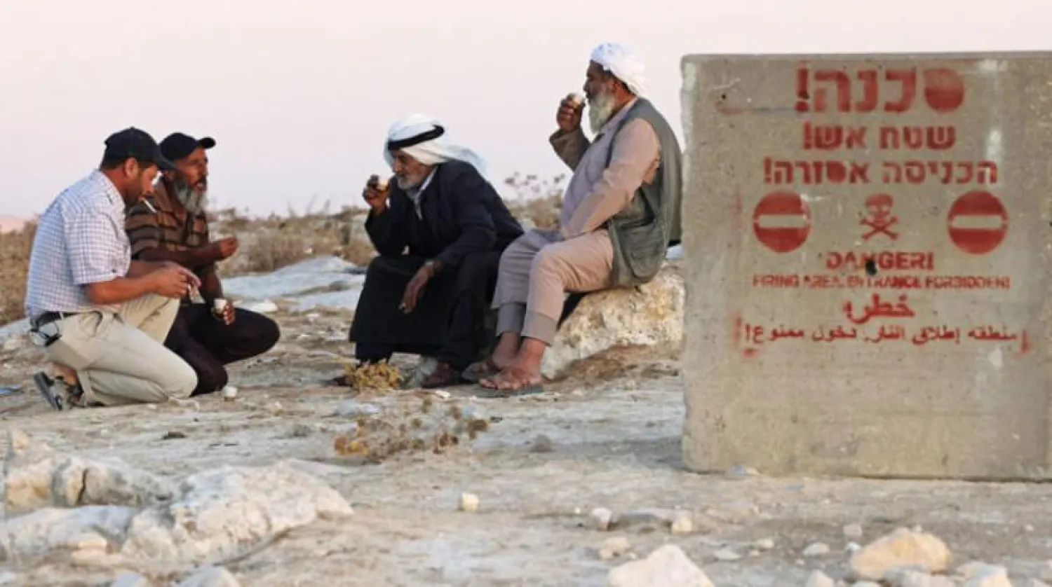 Filistinliler, Batı Şeria’nın güneyindeki Masafer Yatta’da bir atış bölgesine işaret eden İbranice, Arapça ve İngilizce bir tabelanın yanında oturuyorlar (AFP)