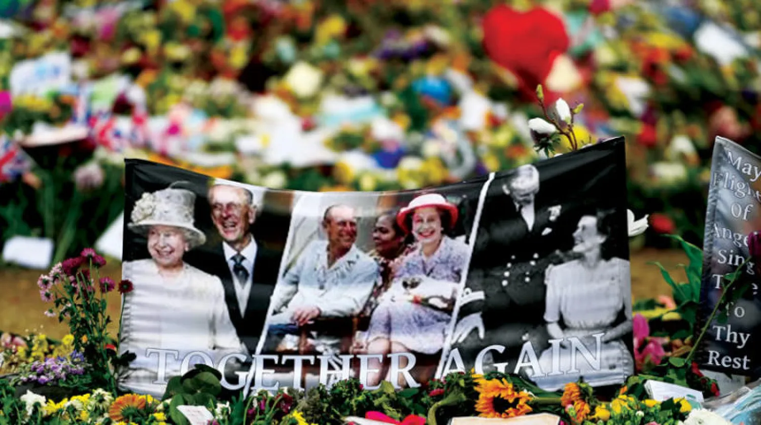 صور للملكة الراحلة وسط باقات ورد خارج قصر باكنغهام في لندن أمس (إ.ب.أ)