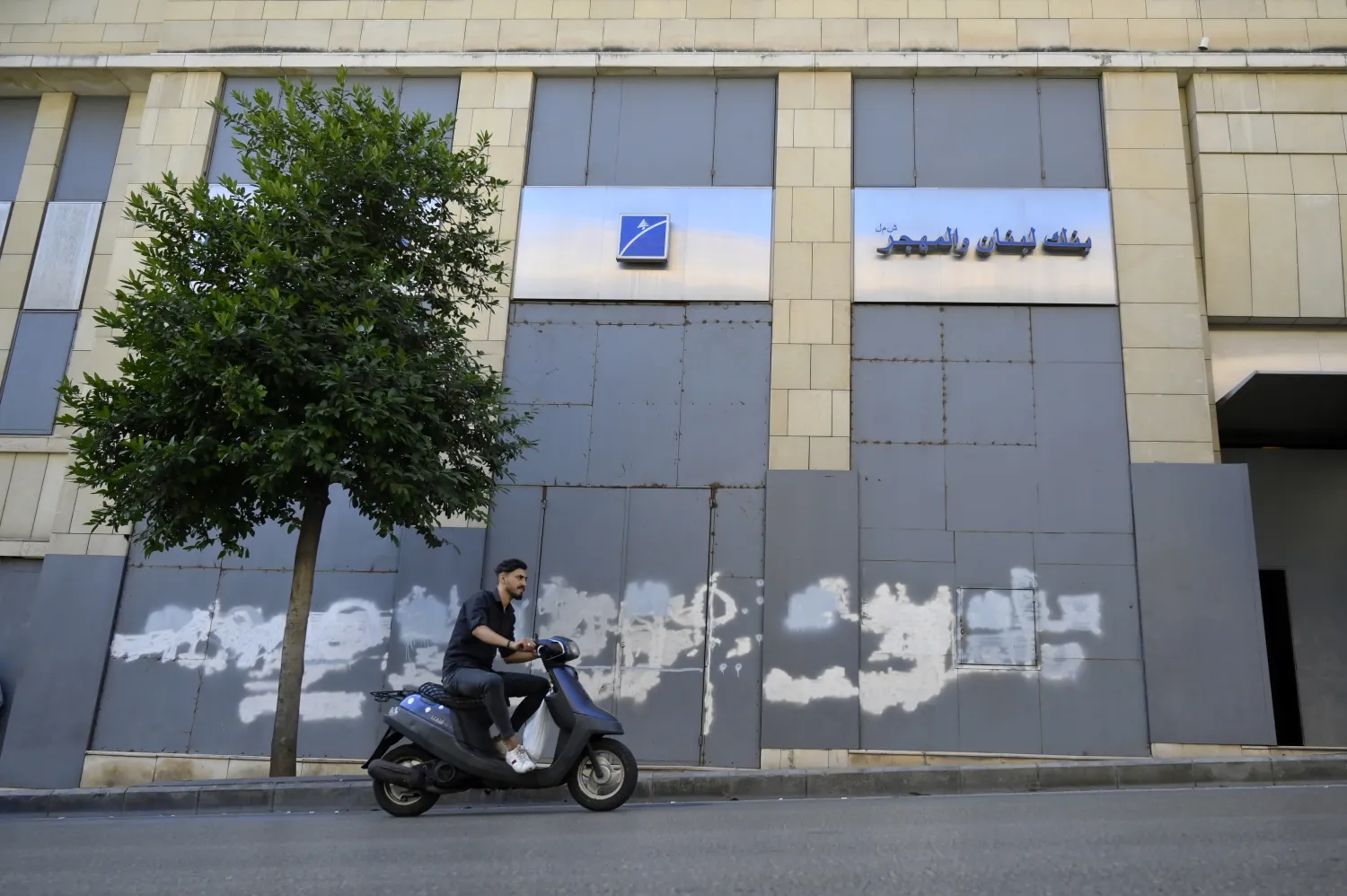 لبناني يقود دراجة نارية أمام مصرف مغلق بعد اقتحامات متكررة للمصارف الأسبوع الماضي (إ.ب.أ)