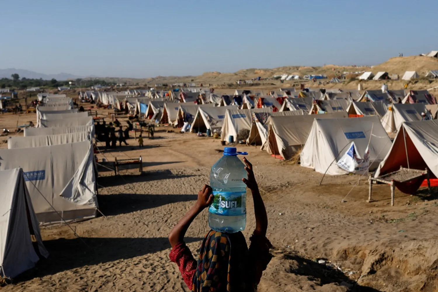 A displaced girl carries a bottle of water she filled from nearby stranded flood-waters, as her family takes refuge in a camp, in Sehwan, Pakistan, September 30, 2022. (Reuters)